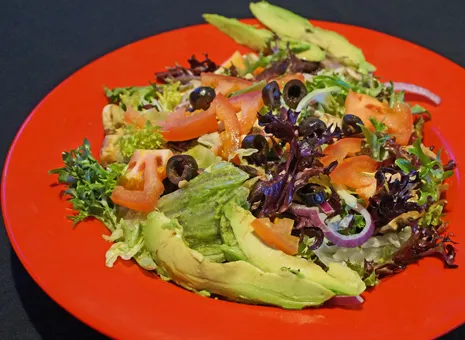 A salad with avocado, tomatoes and black olives.