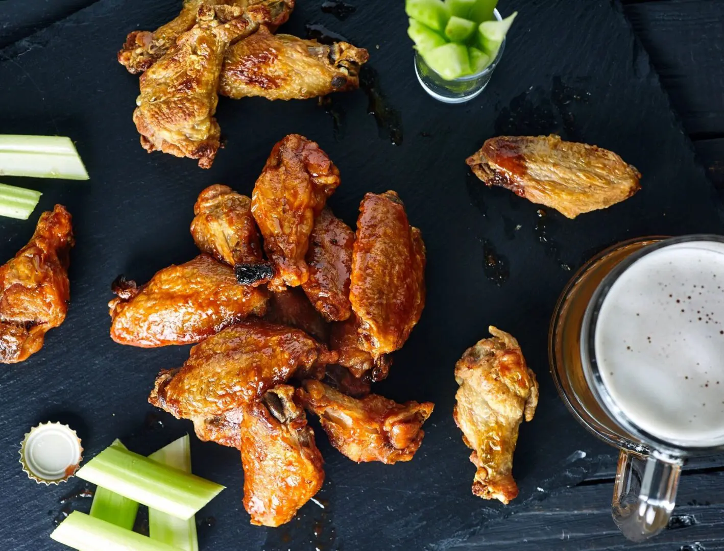 A table topped with lots of chicken wings next to celery.