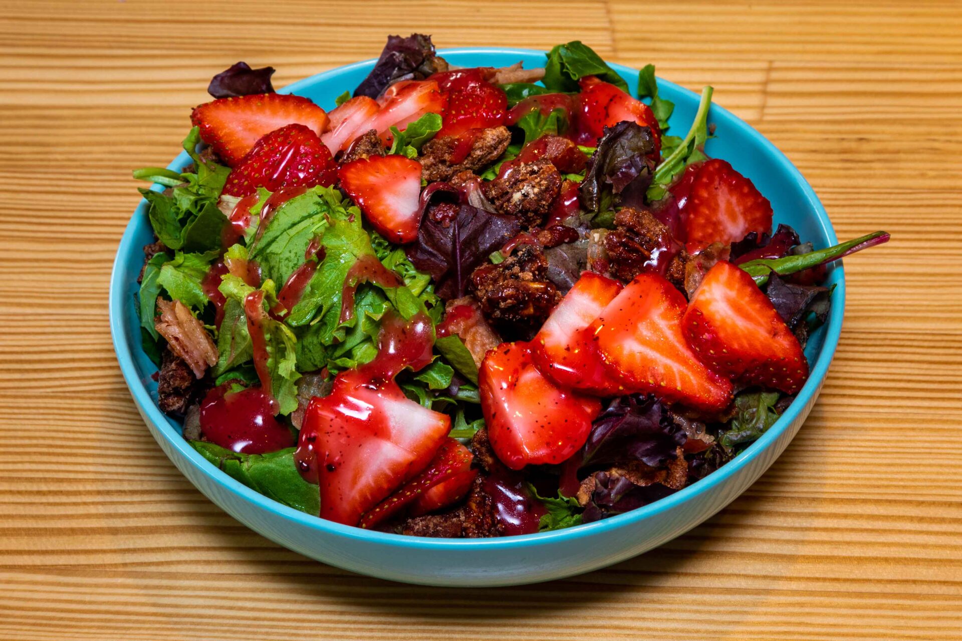 A bowl of salad with strawberries and nuts.
