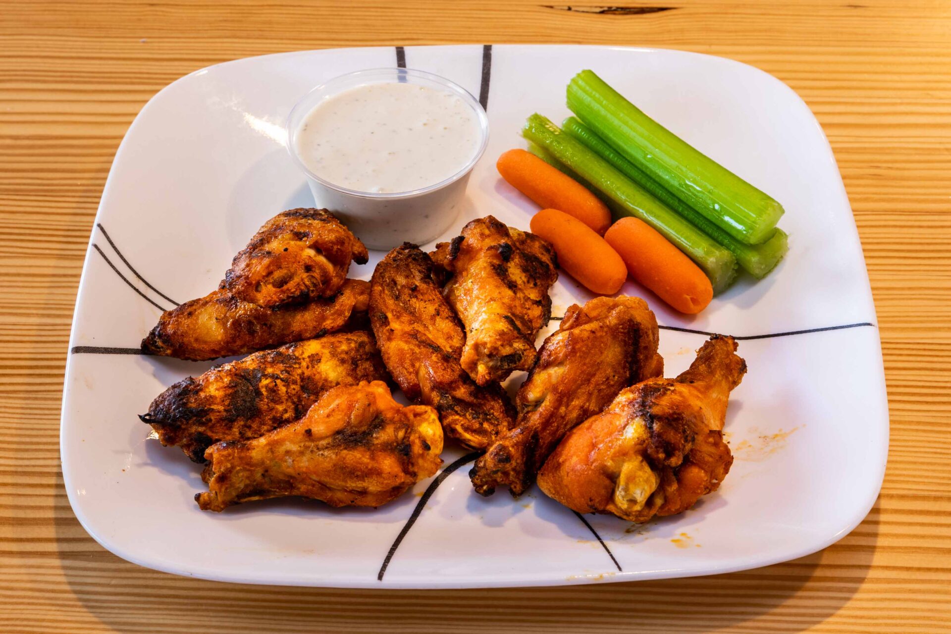 A plate of chicken wings and vegetables on the table.